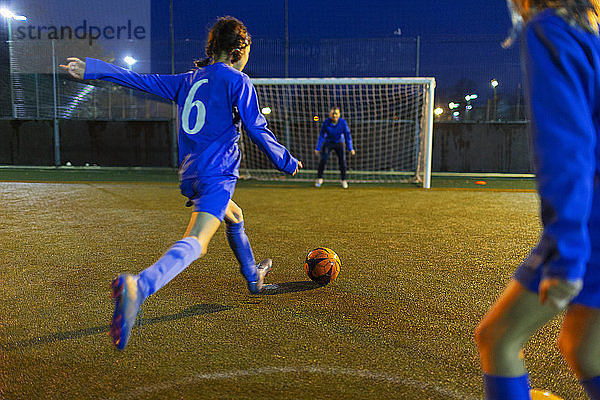Mädchenfußballspieler  der den Ball in Richtung Tor schießt