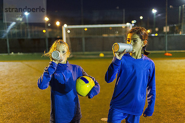 Fußballspielerinnen machen eine Pause und trinken nachts auf dem Spielfeld Wasser