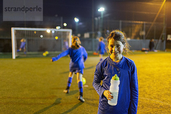 Porträt lächelndes Mädchen Fußballspieler trinken Wasser auf dem Feld in der Nacht