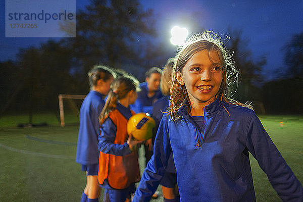 Lächelndes Mädchen spielt Fußball auf einem Feld bei Nacht