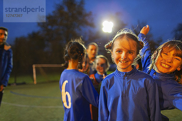 Porträt selbstbewusster  glücklicher Mädchenfußballspieler auf dem Feld bei Nacht