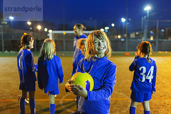 Porträt eines lächelnden  begeisterten Mädchens beim nächtlichen Fußballtraining auf einem Feld