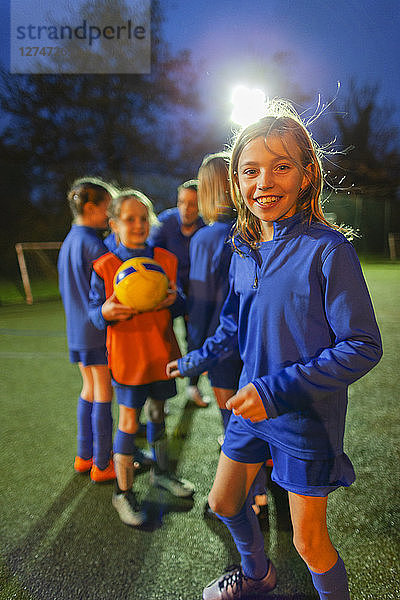 Porträt einer lächelnden  selbstbewussten Fußballspielerin  die mit ihrer Mannschaft auf einem nächtlichen Feld übt