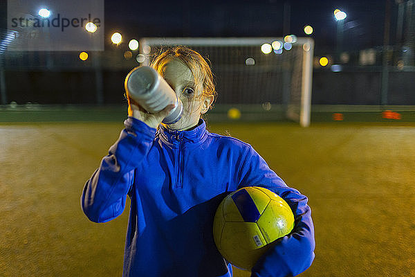 Fußballspielerin macht eine Pause und trinkt nachts auf dem Spielfeld Wasser