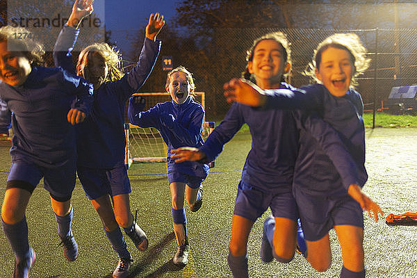Begeisterte Mädchenfußballmannschaft  die nachts auf dem Feld rennt und jubelt