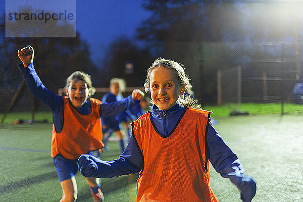 Porträt begeisterter Mädchenfußballerinnen  die nachts auf dem Spielfeld jubeln