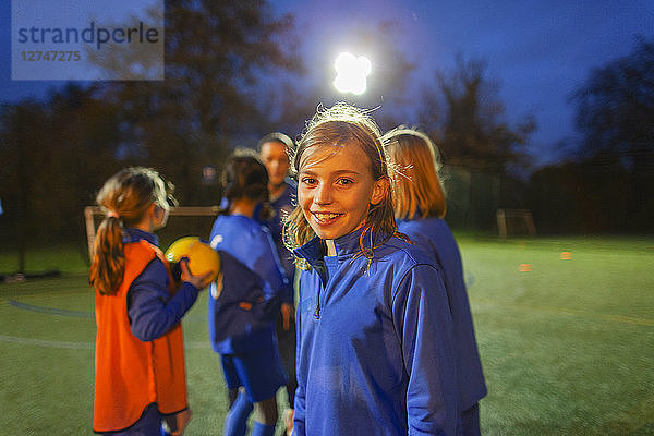 Porträt einer lächelnden  selbstbewussten Fußballspielerin auf einem nächtlichen Spielfeld