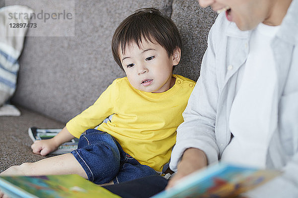 Japanischer Vater und Kind lesen auf dem Sofa
