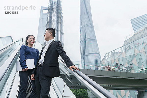 Junge Geschäftsfrau und Mann unterhalten sich beim Aufwärtsfahren auf der städtischen Rolltreppe  Shanghai  China