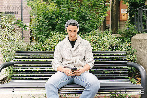 Junger Mann schreibt eine SMS  während er auf einer Bank sitzt  Vancouver  Kanada