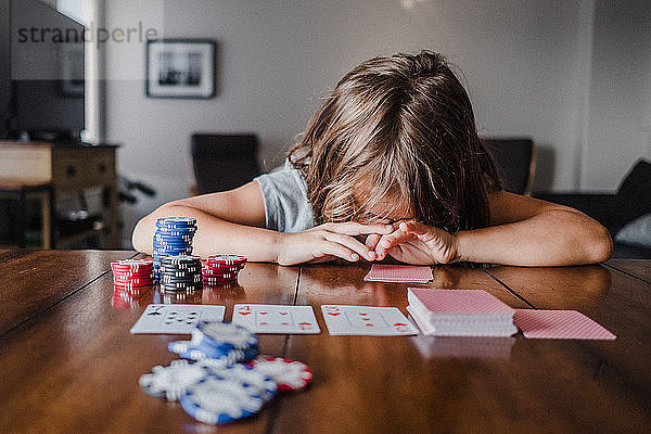 Mädchen spielt Karten am Tisch mit dem Kopf nach unten
