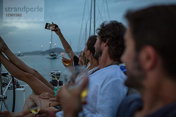 Vier Freunde sitzen in der Abenddämmerung auf dem Boot  trinken Wein  nehmen Selfie  Britische Jungferninseln