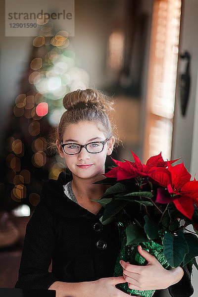 Mädchen hält Weihnachtspoinsettie im Wohnzimmer  Porträt
