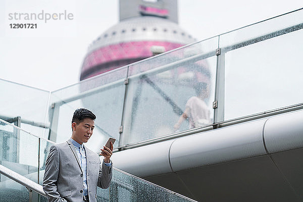 Junger Geschäftsmann betrachtet Smartphone auf Stadttreppe  Shanghai  China