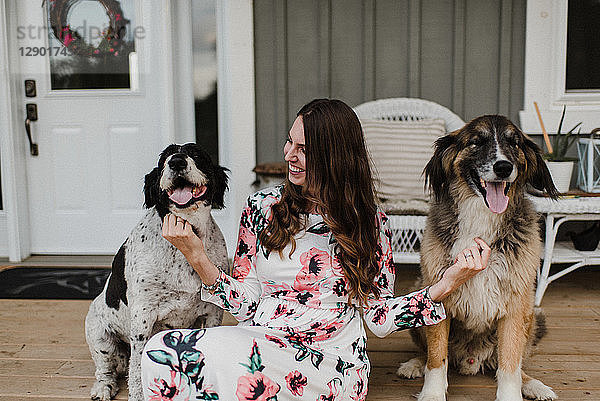Frau und ihre zwei Hunde sitzen auf der Veranda