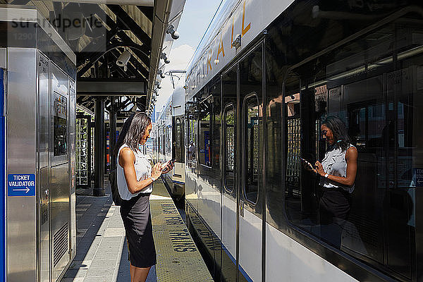 Geschäftsfrau benutzt Handy im Bahnhof