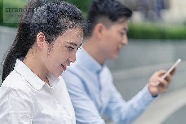 Junge Geschäftsfrau und junger Mann schauen auf Smartphone in der Stadt  Shanghai  China
