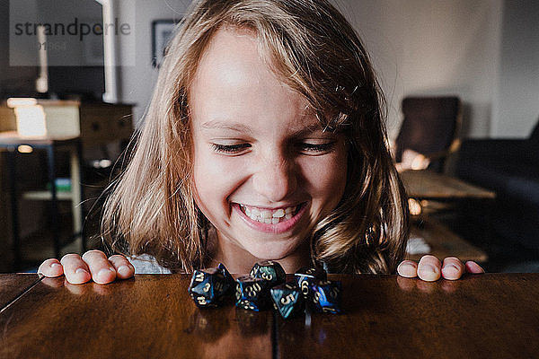 Lächelndes Mädchen am Tisch betrachtet Rollenspielwürfel  Nahaufnahme