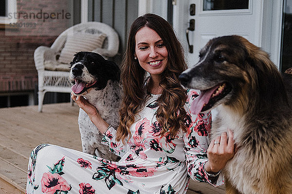 Frau und ihre zwei Hunde sitzen auf der Veranda