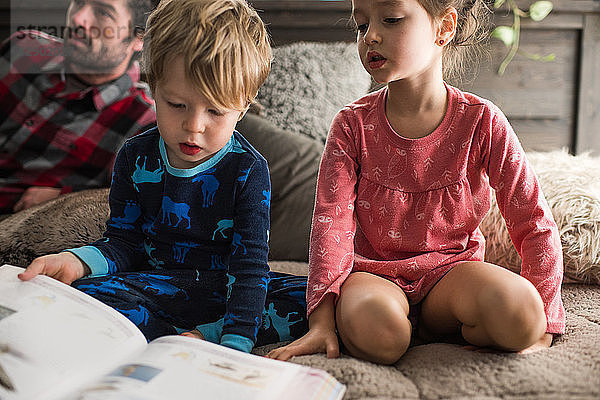 Kinder  die zu Hause ein Buch lesen  Vater im Hintergrund