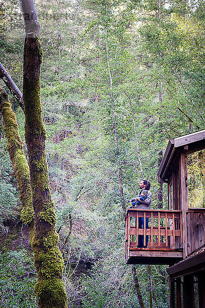 Vater mit kleinem Sohn auf dem Balkon eines Holzstelzenhauses im Wald  Cazadero  Kalifornien  USA