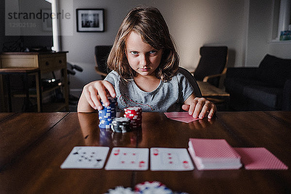 Mädchen mit einem Stapel Spielchips  die am Tisch Karten spielt  Portrait