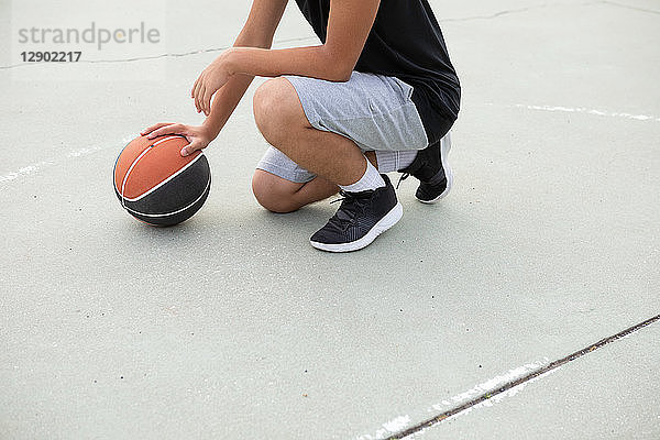 Männlicher jugendlicher Basketballspieler hockt mit dem Ball auf dem Basketballfeld  Hals nach unten