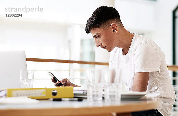 Teenager-Schüler am Schreibtisch im Klassenzimmer mit Blick auf Smartphone