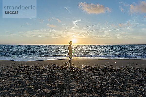 Mann geht bei Sonnenuntergang am Strand spazieren