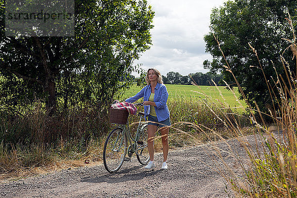 Reife Frau schiebt Fahrrad auf ländlicher Straße