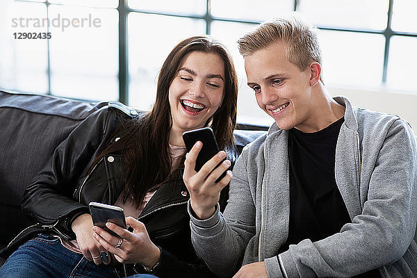 Teenager  Mädchen und Junge sitzen auf dem Sofa und schauen auf ein Smartphone