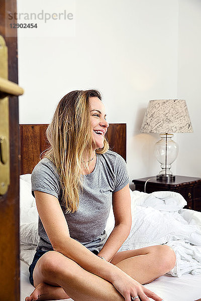 Mittlere erwachsene Frau sitzt lachend auf dem Bett