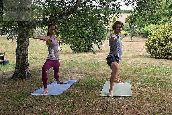 Mann und Frau machen Yoga im Garten  üben die Kriegerhaltung