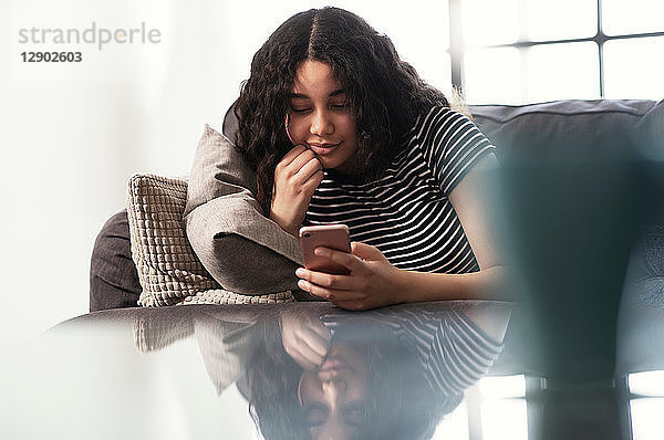 Teenagerin sitzt auf Sofa und schaut auf Smartphone