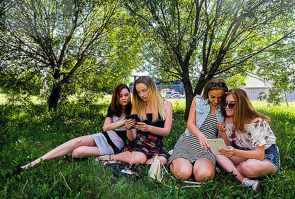 Freundinnen entspannen sich  nutzen intelligente Geräte im Stadtpark