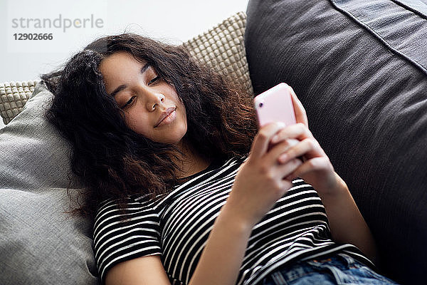 Teenagerin entspannt sich auf Sofa und schaut auf Smartphone