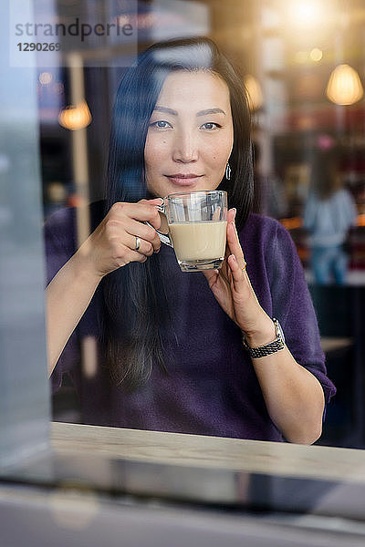 Mittelgroße erwachsene Frau mit Kaffee  die vom Fensterplatz des Cafés hinaussieht  Porträt