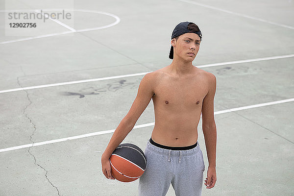 Männlicher jugendlicher Basketballspieler mit Ball auf Basketballfeld  Porträt