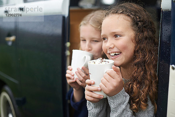 Mädchen trinken heiße Schokolade neben dem Wohnmobil