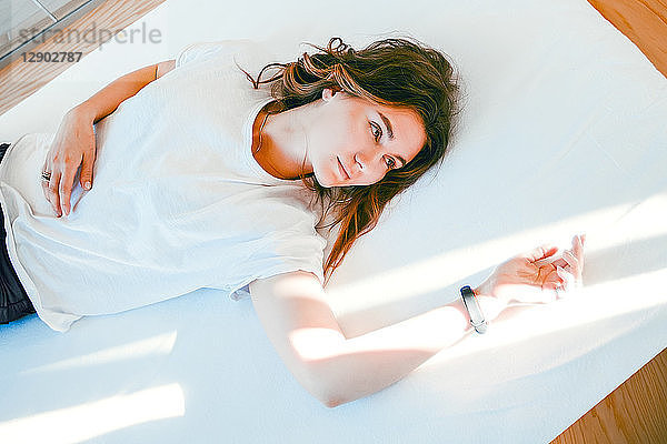 Junge Frau entspannt auf dem Bett  den Arm im Lichtstrahl ruhend  nachdenklicher Ausdruck