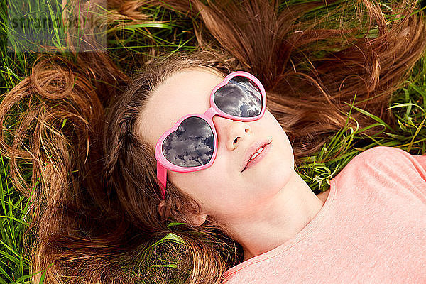 Mädchen mit herzförmiger Sonnenbrille auf Gras liegend