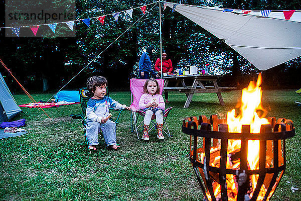 Kinder entspannen sich vor dem Lagerfeuer  die Eltern im Hintergrund