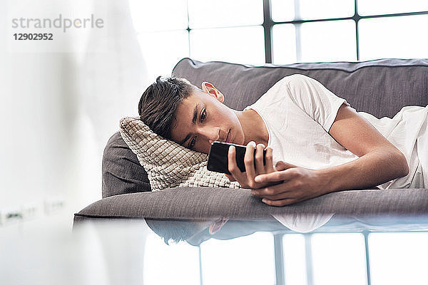 Teenager Junge liegt auf Sofa und schaut auf Smartphone