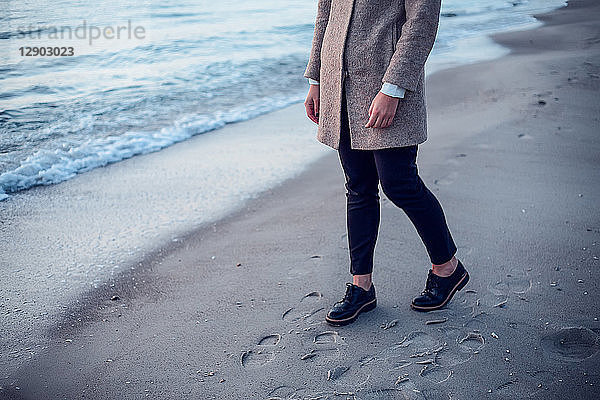 Junge Frau geht am Strand spazieren  hinterlässt Fußspuren im nassen Sand  niedriger Abschnitt