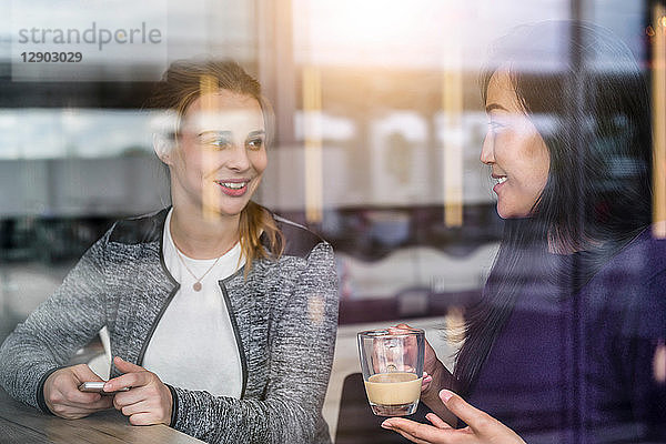 Zwei Studentinnen trinken Kaffee am Fensterplatz eines Cafés