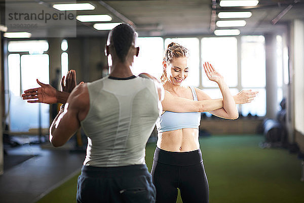 Trainerin und Klientin machen Dehnungsübungen im Fitnessstudio