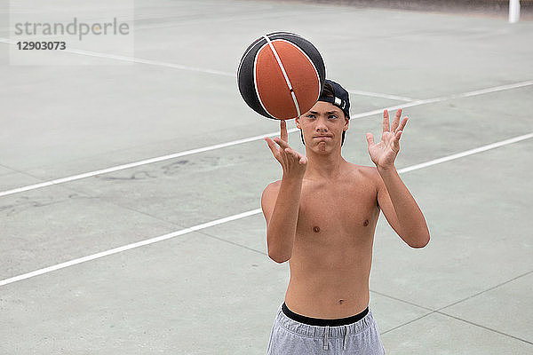 Männlicher Teenager-Basketballspieler  der den Ball auf dem Basketballfeld auf dem Finger dreht