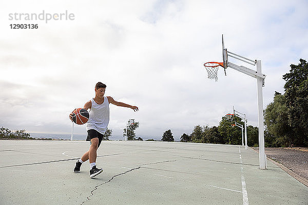 Männlicher jugendlicher Basketballspieler läuft mit dem Ball auf dem Basketballfeld
