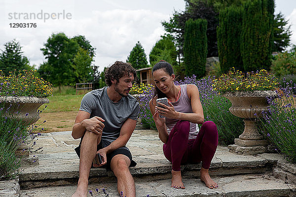 Mann und Frau üben Yoga im Garten und schauen sich auf der Terrasse Smartphones an