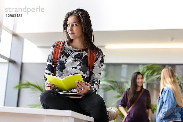 Junge Studentin liest Buch in der Lobby der Universität